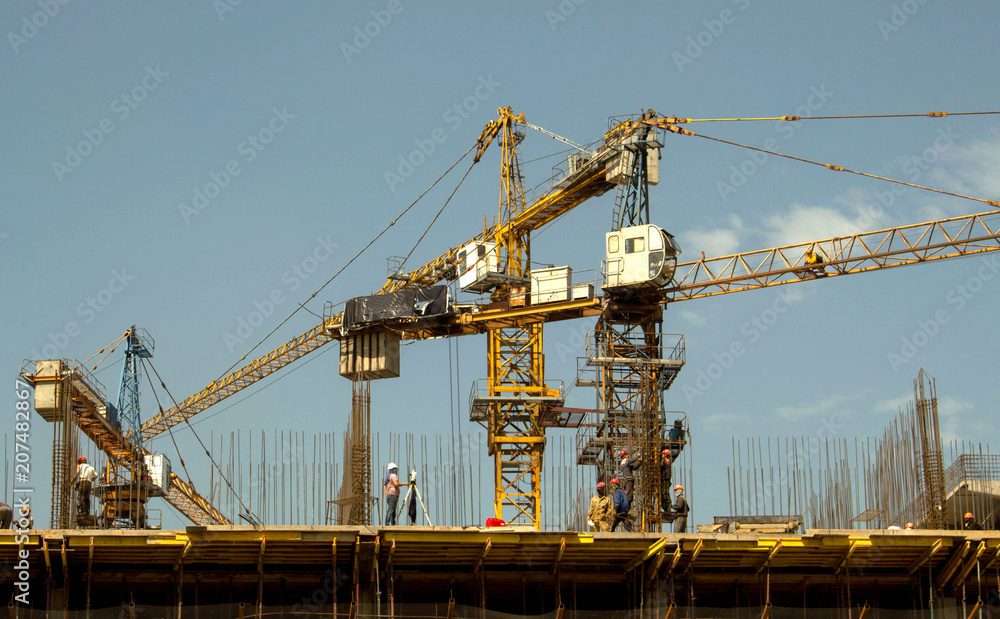  building, people in helmets, tower cranes against the sky
