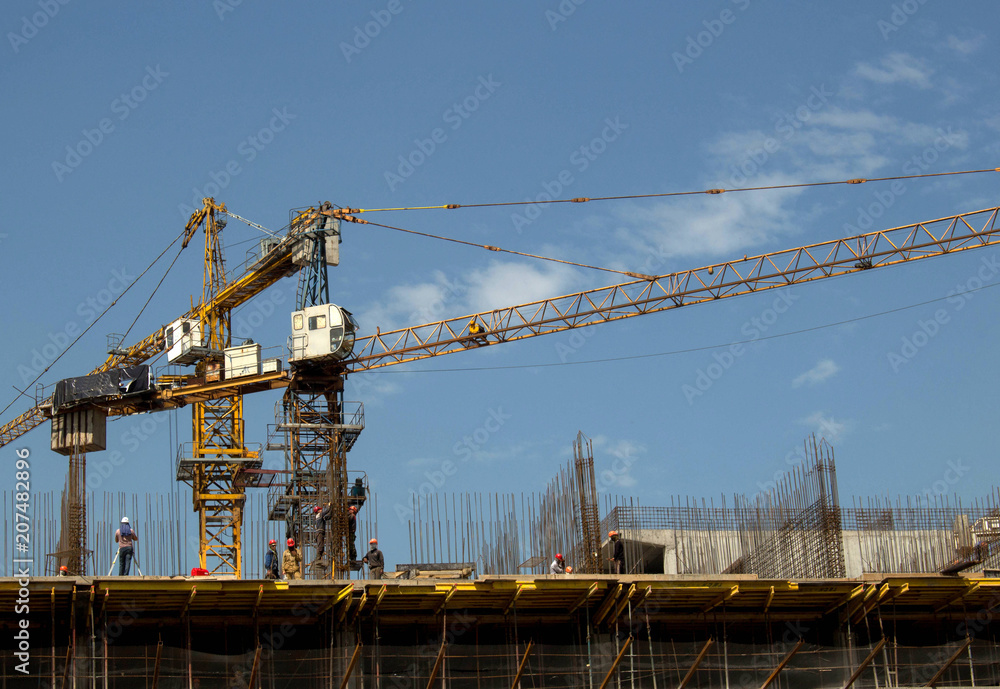 building, people in helmets, tower cranes against the sky
