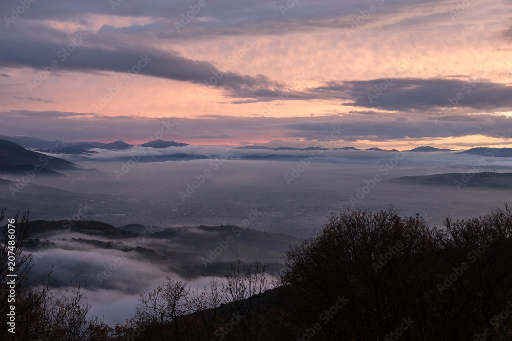 Umbria valley in winter filled by mist at sunset, with emerging 