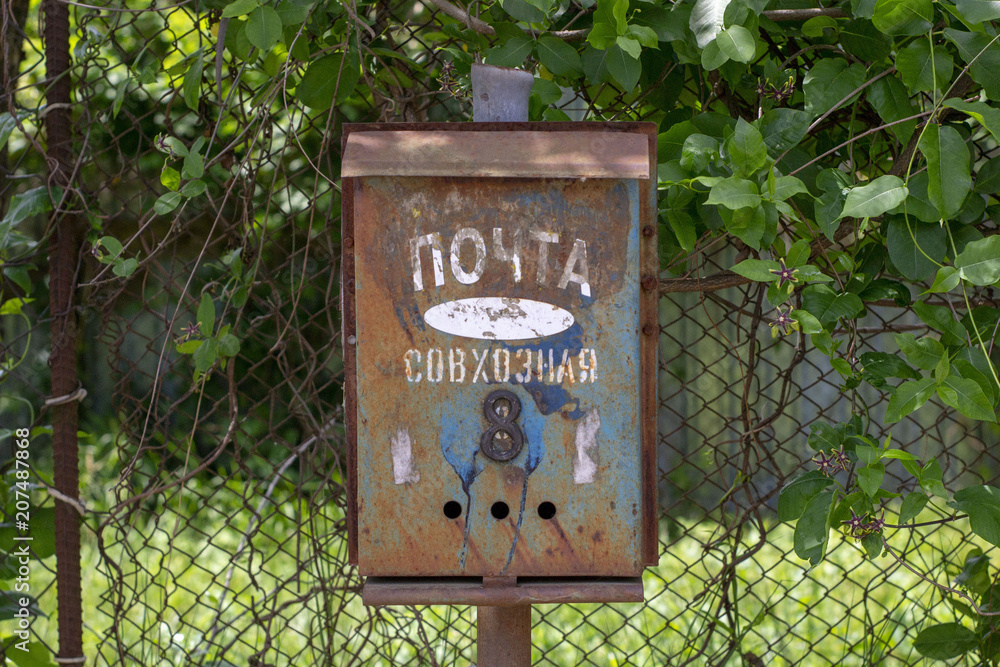 Simple still-life photo of old rust mail box in village near metal fence and ivy Simple still-life photo of old rust mail box in village near metal fence and ivy