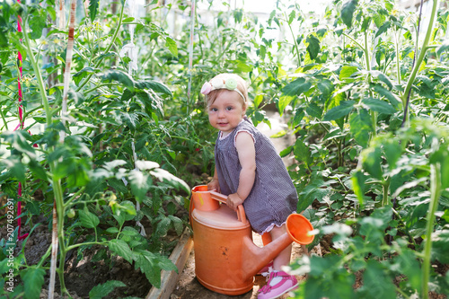 Little girl with watering can is among green plants in a garden