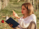 Girl reading a book sitting in the nature with a fallen leaf in her hand