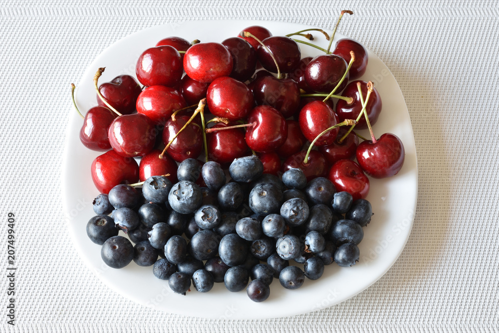 Fresh sweet red cherries with blue bilberries on a white plate, closeup Fresh sweet red cherries with blue bilberries on a white plate, closeup