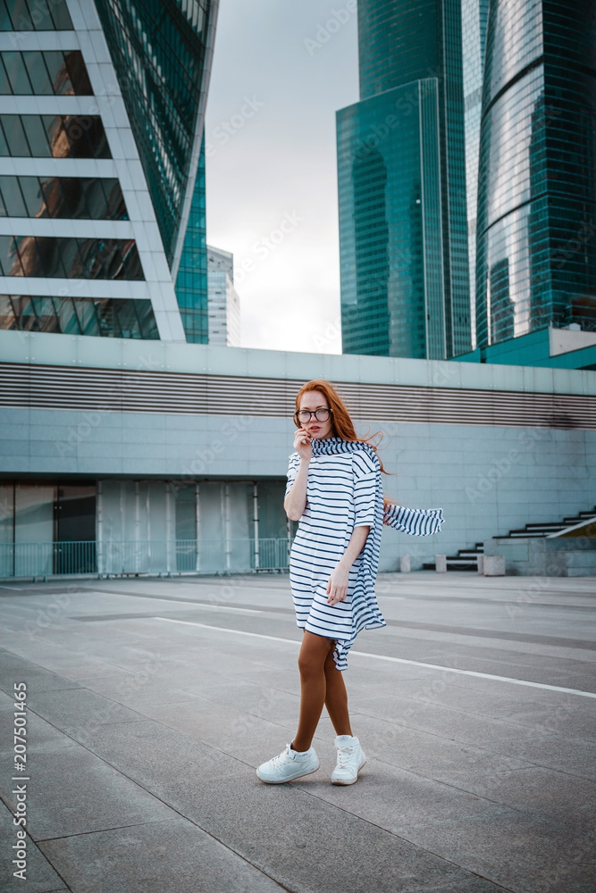 Smiling beautiful woman in a light coat against the backdrop of a skyscrapers business center of a big city Smiling beautiful woman in a light coat against the backdrop of a skyscrapers business center of a big city