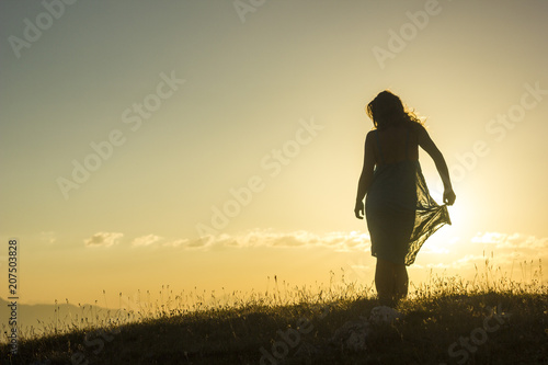 silhouete of girl in dress standing on grass in sunset mountains