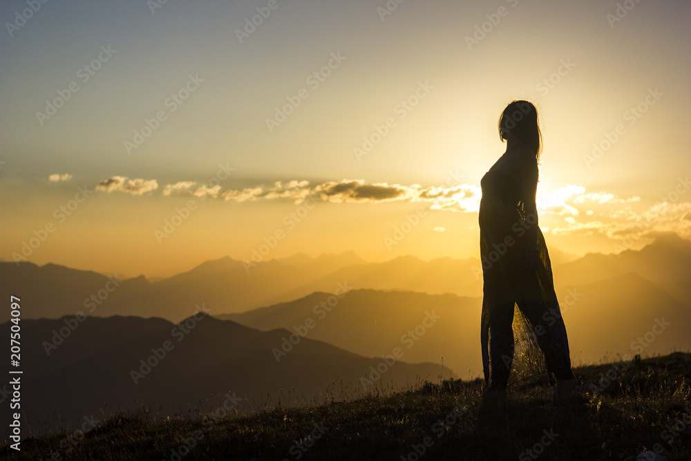 silhouete of girl in dress standing on grass in sunset mountains silhouete of girl in dress standing on grass in sunset mountains