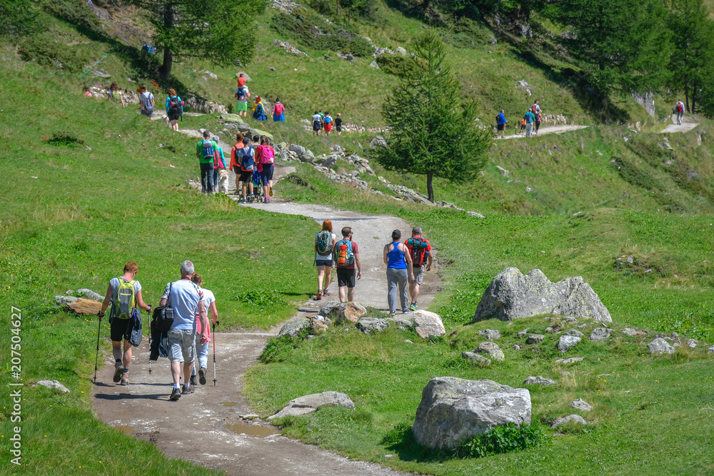Group of People with backpacks walking on a mountain path. A beautiful sunny day to trekking with family and friends climbing to the mountains for an excursion in nature. Enjoying a summer day.