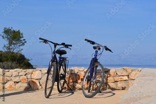 Fototapeta Naklejka Na Ścianę i Meble -  Two bikes against a wall with an ocean backdrop