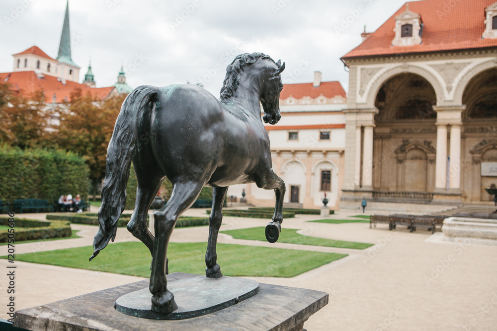 A statue of a horse in the Waldstein Garden in Prague in the Czech Republic. In the background are architectural buildings A statue of a horse in the Waldstein Garden in Prague in the Czech Republic. In the background are architectural buildings
