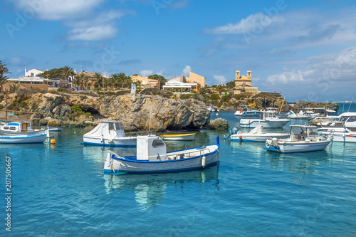 Boats in the port on a sunny summer day, you can see the yellow rocks, palms and houses. Tabarca Island in Spain.