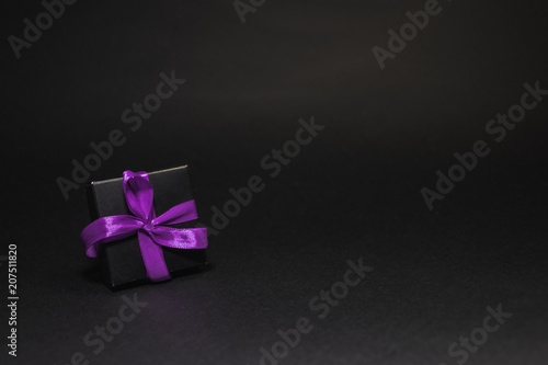 black box tied with purple ribbon on a black background
