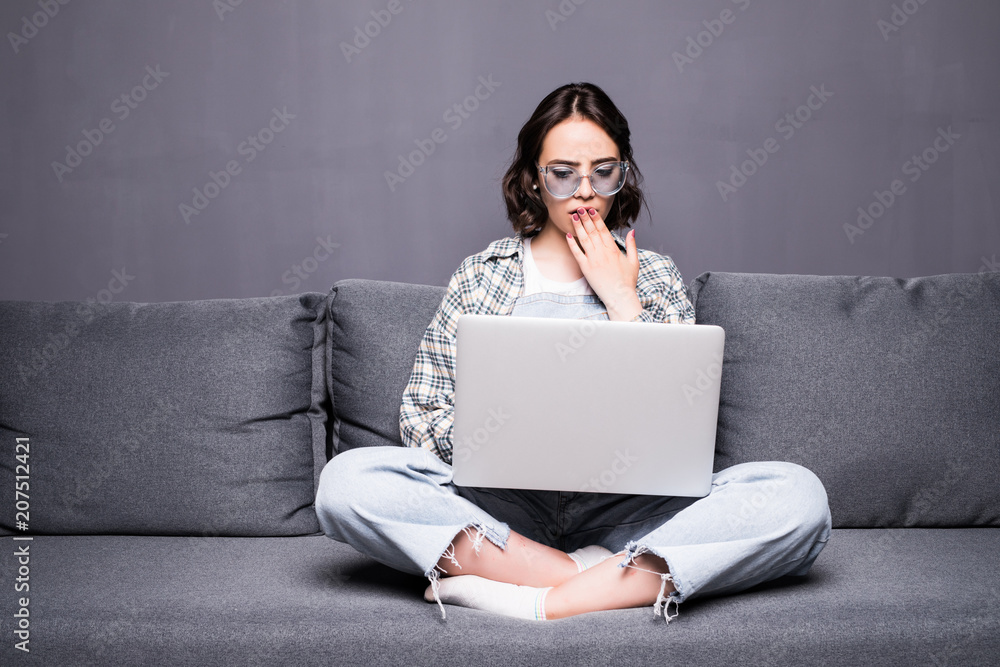 Naklejka premium Young beautiful woman with glasses using a laptop computer at home sitting on sofa