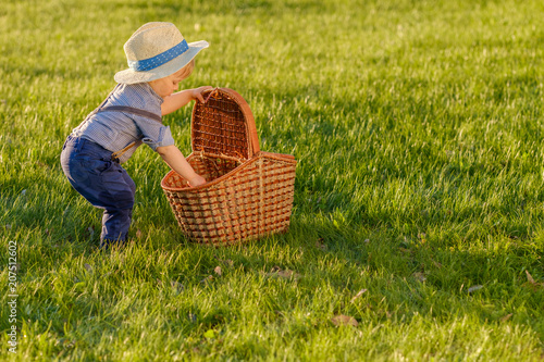Toddler child outdoors. One year old baby boy wearing straw hat looking in picnic basket