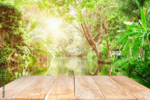 Empty wooden desk of free space and spring time with Morning sun light with wind blowing leaves in the lake park Template mock up for display montages of product.