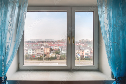 Home window with blue curtain and view to residential suburban building exterior on blue sky background. © svetlana