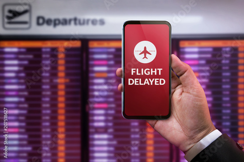 Modern Technology in Travel Concept. Flight Delayed on Smartphone Screen. Businessman using Mobile Phone in front of Departures Board to Re-Checked Flight Information in Airport