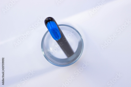 Black style toothbrushes wiht blue bristle in glass on table on lwhite moning background, top view
