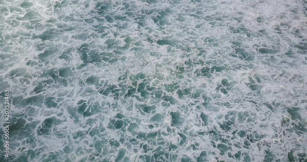 Drone flying over foaming waves breaking in open blue sea, revealing cloudy horizon. Beautiful ocean foam background.