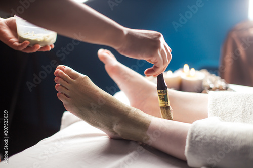 Close up of spa worker female hands aplying mad clay mask on female client foot in salon. photo