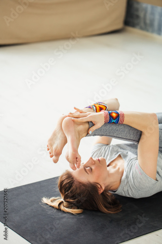 Young woman practicing yoga in loft interior, doing stretching warmup, n mat, supta paschimottanasana. photo