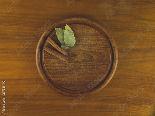 Round wooden cutting board with nutmeg, cinnamon, and bay leaves resting on a wooden table
