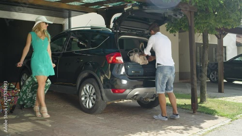 SLOW MOTION, LENS FLARE: Young couple argues after woman packs too much luggage for their summer holiday. Man loading travel bags into the black SUV gets angry with his girlfriend for overpacking. photo