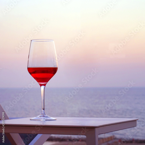 A glass of red wine standing on a table a background of a sea horizon at sunset. A glass of red wine against the background of the evening sea horizon.