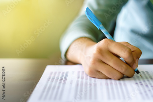 Close up of high school or university student holding a pen writing on answer sheet paper in examination room. College students answering multiple choice questions test in testing room in university. photo