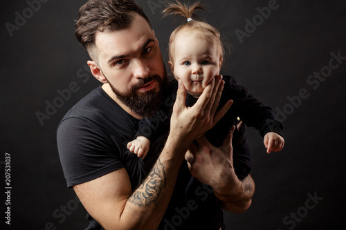 Father and infant daughter posing with different funny grimaces at studio black background with copyspace. Close up. Happy Dad hugging amasing beautiful and funny little baby girl. photo