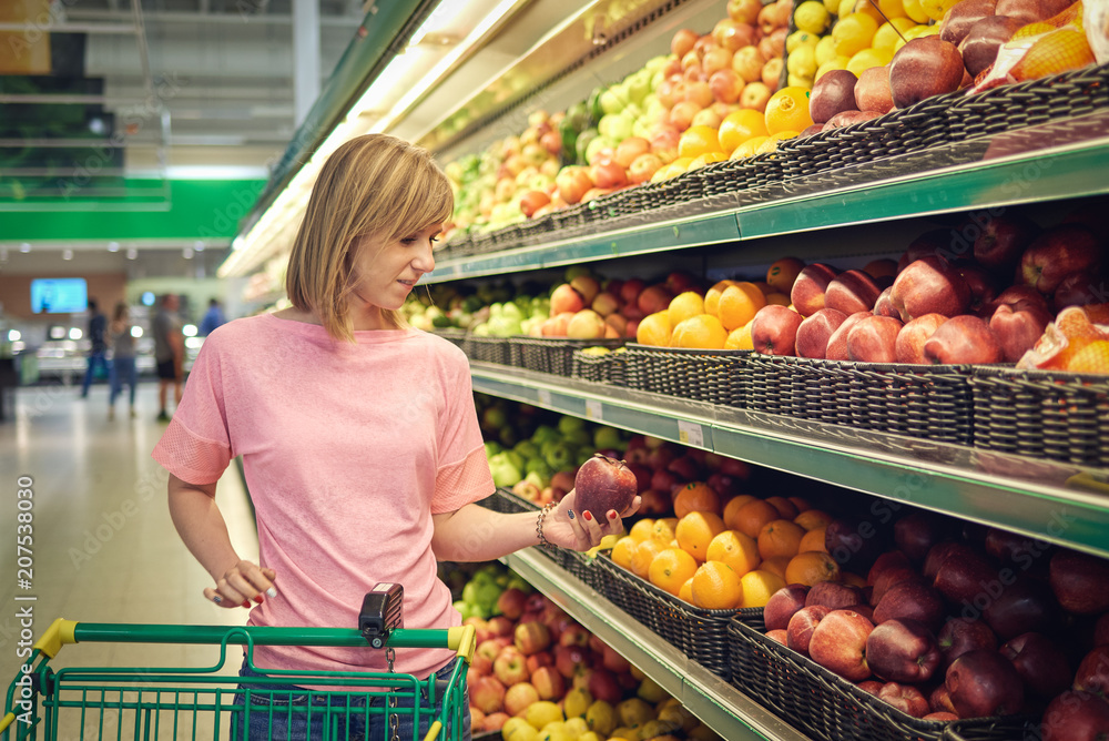 Slender woman standing in front of a row of produce in a grocery store.