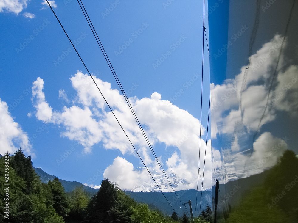 Train in Switzerland alps with reflection of trees, sky and mountains during summer