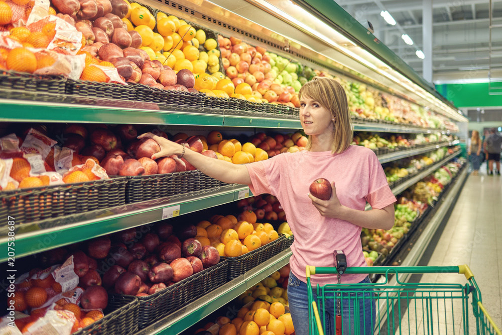 Slender woman standing in front of a row of fruits in a grocery store.