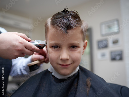 Barber making a haircut to a boy with cutting machine.
