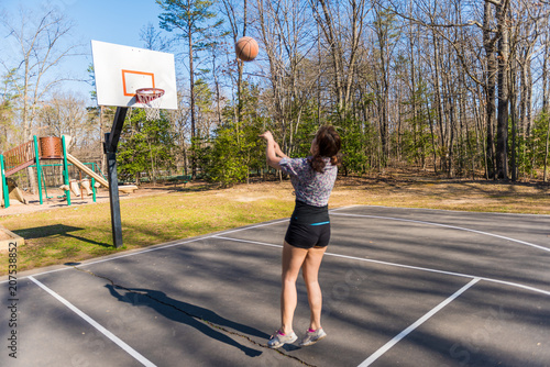 Young fit woman jumping up throwing basketball into hoop in playground