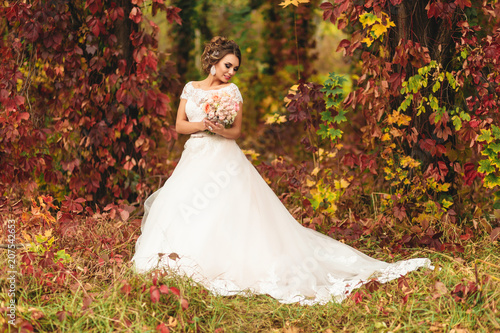 The bride stands in the autumn park and holds a bouquet in her hands. natural background. fairytale forest