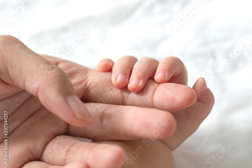 Baby uses his tiny fingers to hold his mother's finger to make him feeling her love, warm, comfort and secure.