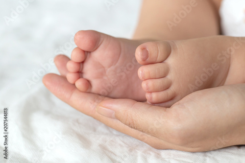 Mother uses her hand to hold her baby's tiny feet to make him feeling her love, warm, comfort and secure.