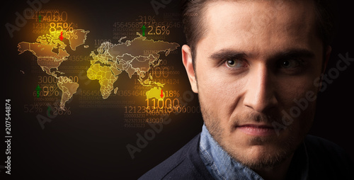 Portrait of a young businessman with a world map and numbers next to him on a dark background