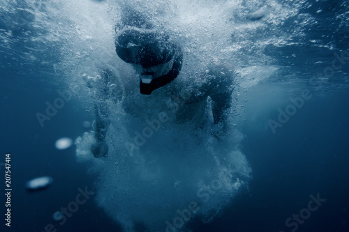 Man snorkeling underwater surface among air bubbles.