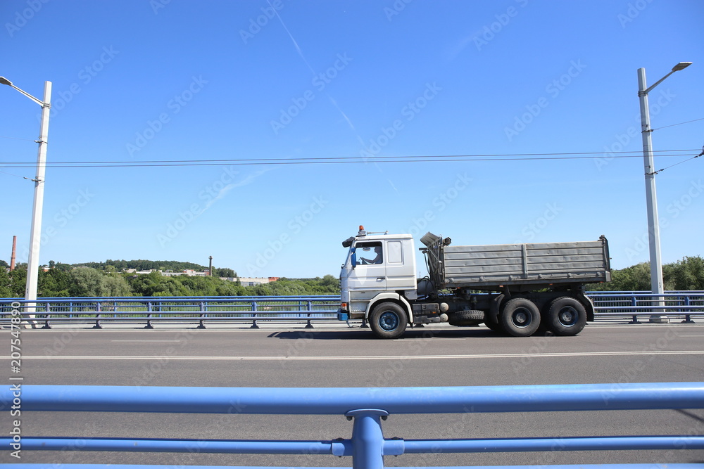 Fototapeta premium Dump truck crossing bridge. Dump truck moving on road against blue barrier or guard rail.