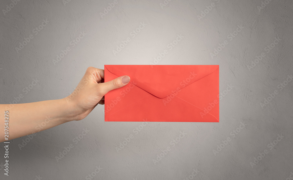 Female hand holding coloured and white envelope with empty wall background
Female hand holding coloured and white envelope with empty wall background