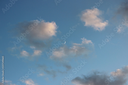 a thin crescent in the early evening is visible in the sky among the white clouds © wolfness72