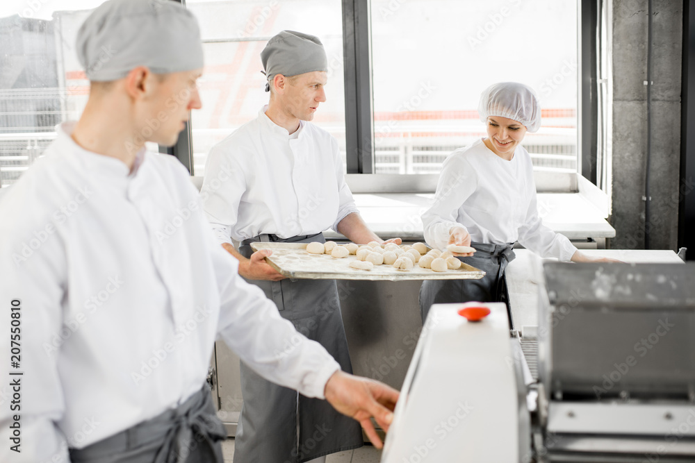 Bakers in uniform working with dough rolling machine making buns at the bakery manufacturing Bakers in uniform working with dough rolling machine making buns at the bakery manufacturing