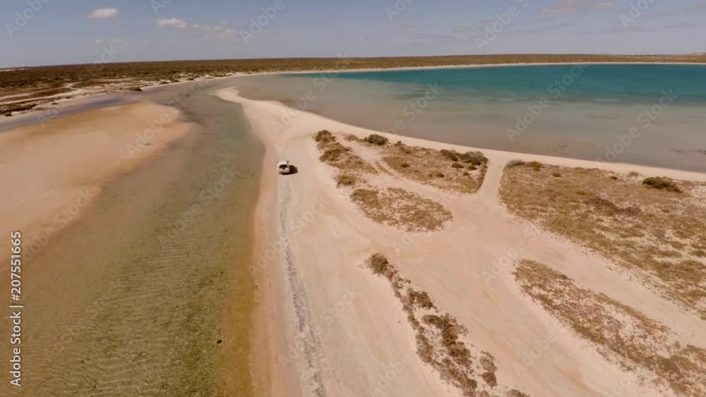 An aerial shot of a coast and sea with a ute driving on lands An aerial shot of a coast and sea with a ute driving on lands