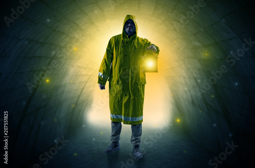 Ugly man in raincoat walking with glowing lantern in a dark tunnel