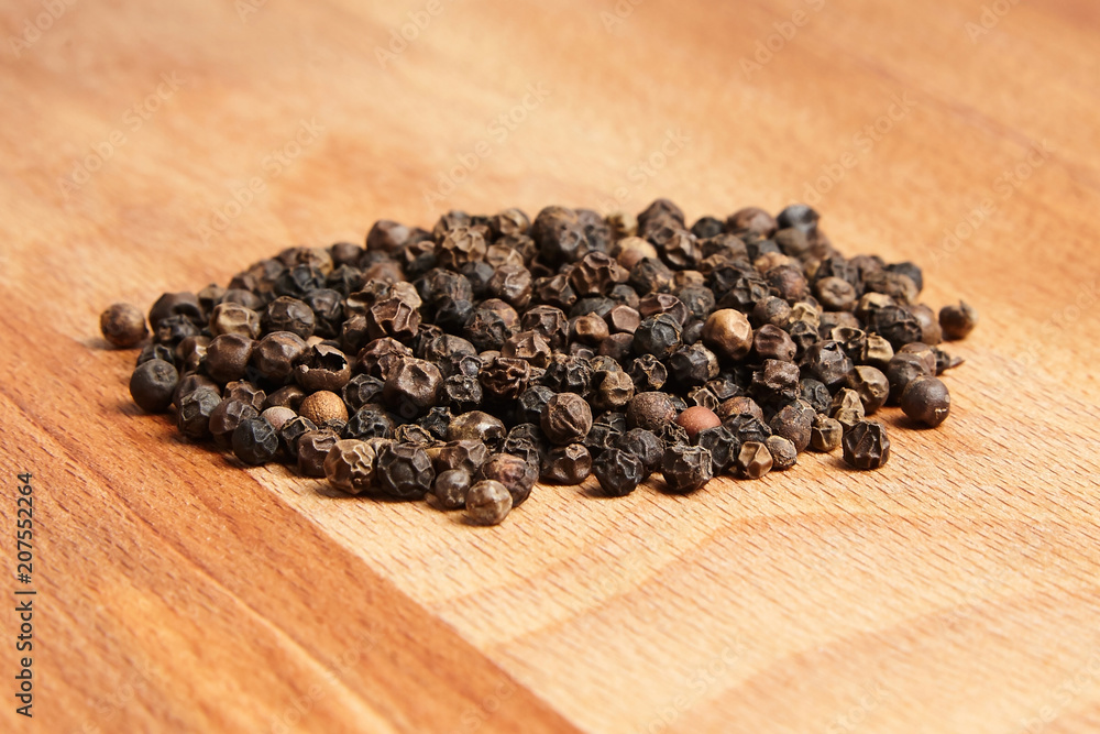 Heap of black peppercorns on wooden beech cutting board Heap of black peppercorns on wooden beech cutting board