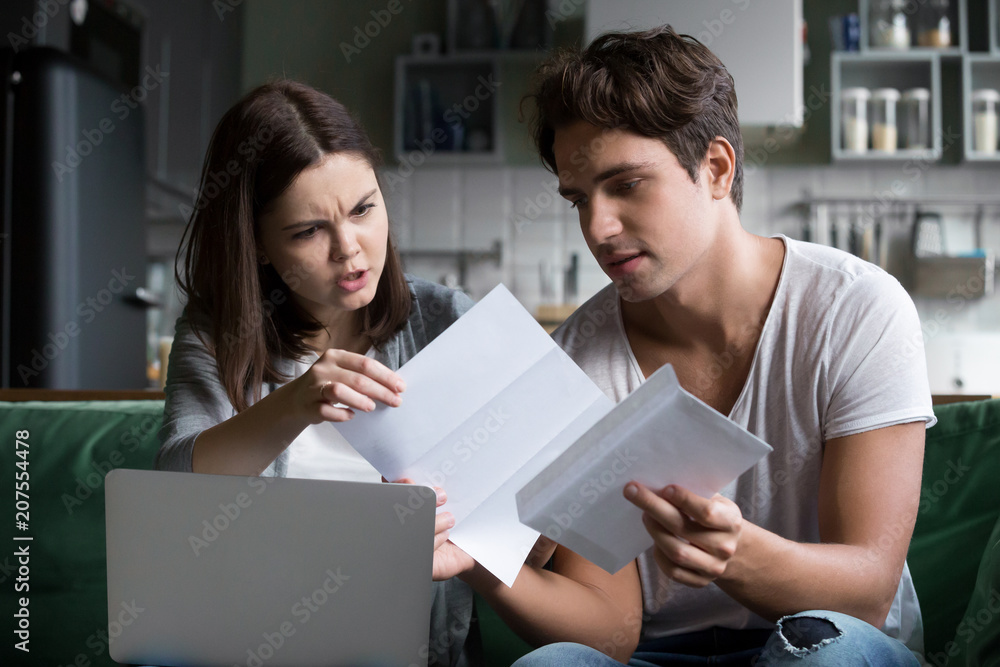 Frustrated wife shocked by bad news, high taxes, final notice past due debt reading mail paper letter from bank with husband at home, millennial couple angry with financial problems, domestic bills Frustrated wife shocked by bad news, high taxes, final notice past due debt reading mail paper letter from bank with husband at home, millennial couple angry with financial problems, domestic bills
