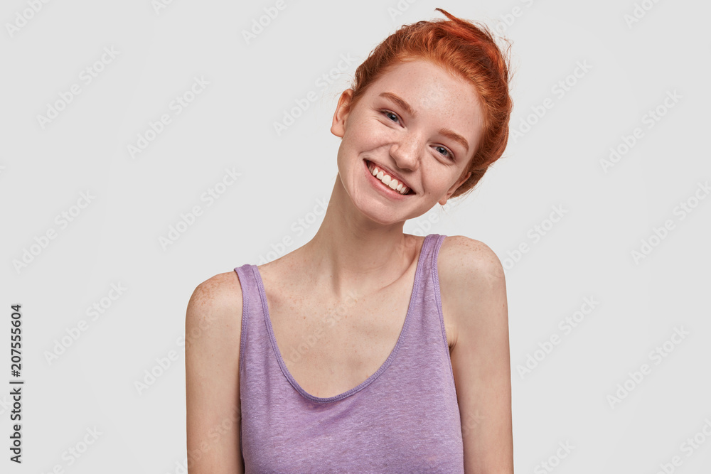 Cheerful young female has charming smile, bends head aside, dressed in casual purple t shirt, listens pleasant story from someone, isolated on white background. Pretty happy ginger woman indoor Cheerful young female has charming smile, bends head aside, dressed in casual purple t shirt, listens pleasant story from someone, isolated on white background. Pretty happy ginger woman indoor