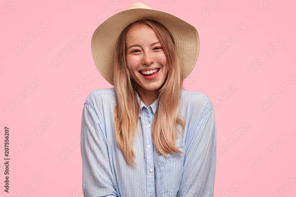 Glad female tourist wears shirt and straw summer hat, smiles happily at camera, being in good mood as ready to flight abroad, poses against pink background. Caucasian woman has unforgettable rest Glad female tourist wears shirt and straw summer hat, smiles happily at camera, being in good mood as ready to flight abroad, poses against pink background. Caucasian woman has unforgettable rest