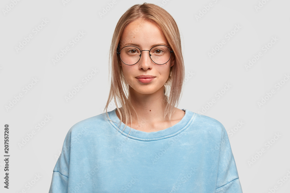 Headshot of attractive Caucasian female looks directly at camera, has no make up, healthy skin, wears big glasses and boyfriend`s sweater, spends spare time together with lover. Beauty, lifestyle Headshot of attractive Caucasian female looks directly at camera, has no make up, healthy skin, wears big glasses and boyfriend`s sweater, spends spare time together with lover. Beauty, lifestyle